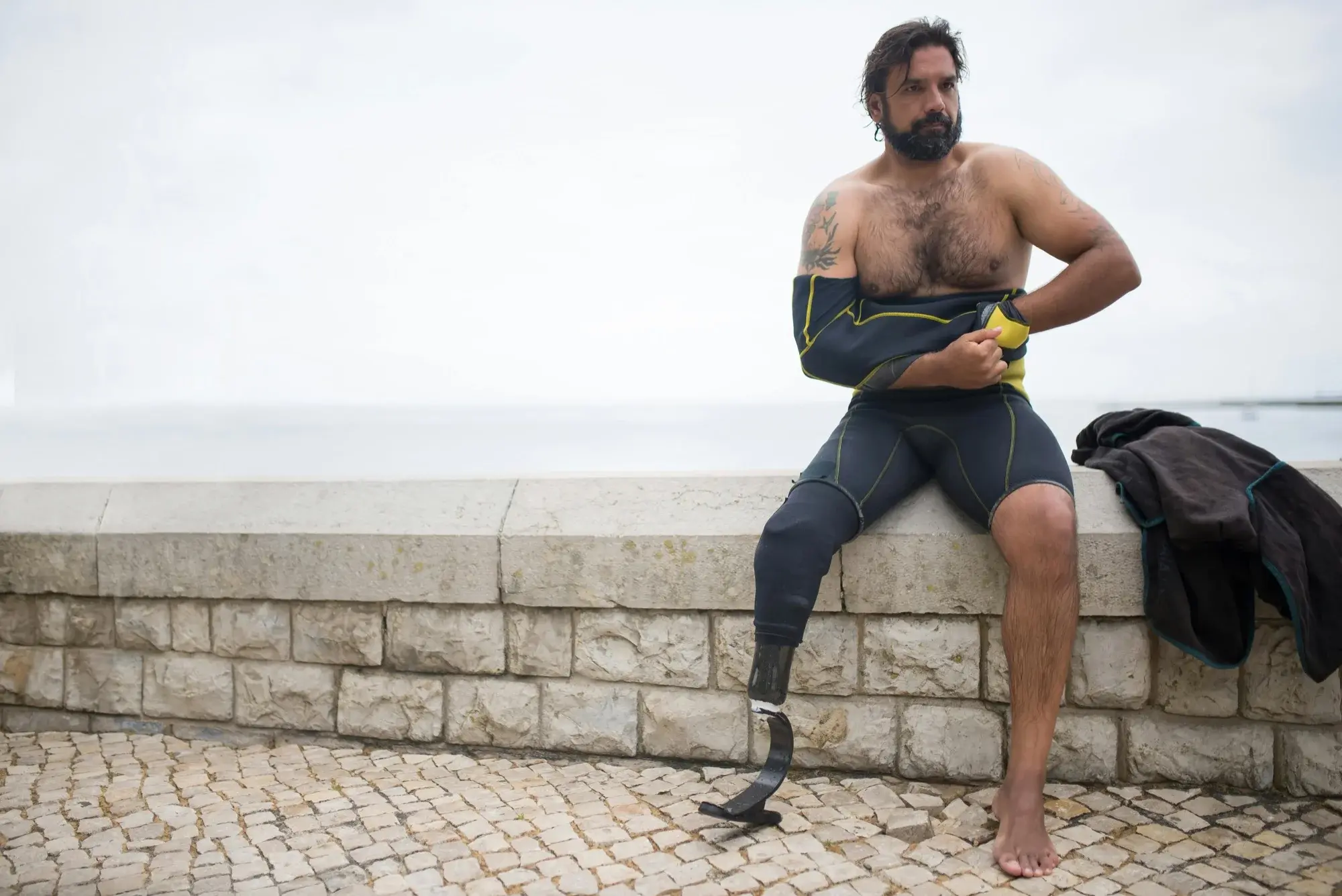 A man with a running prosthesis seated beside the sea