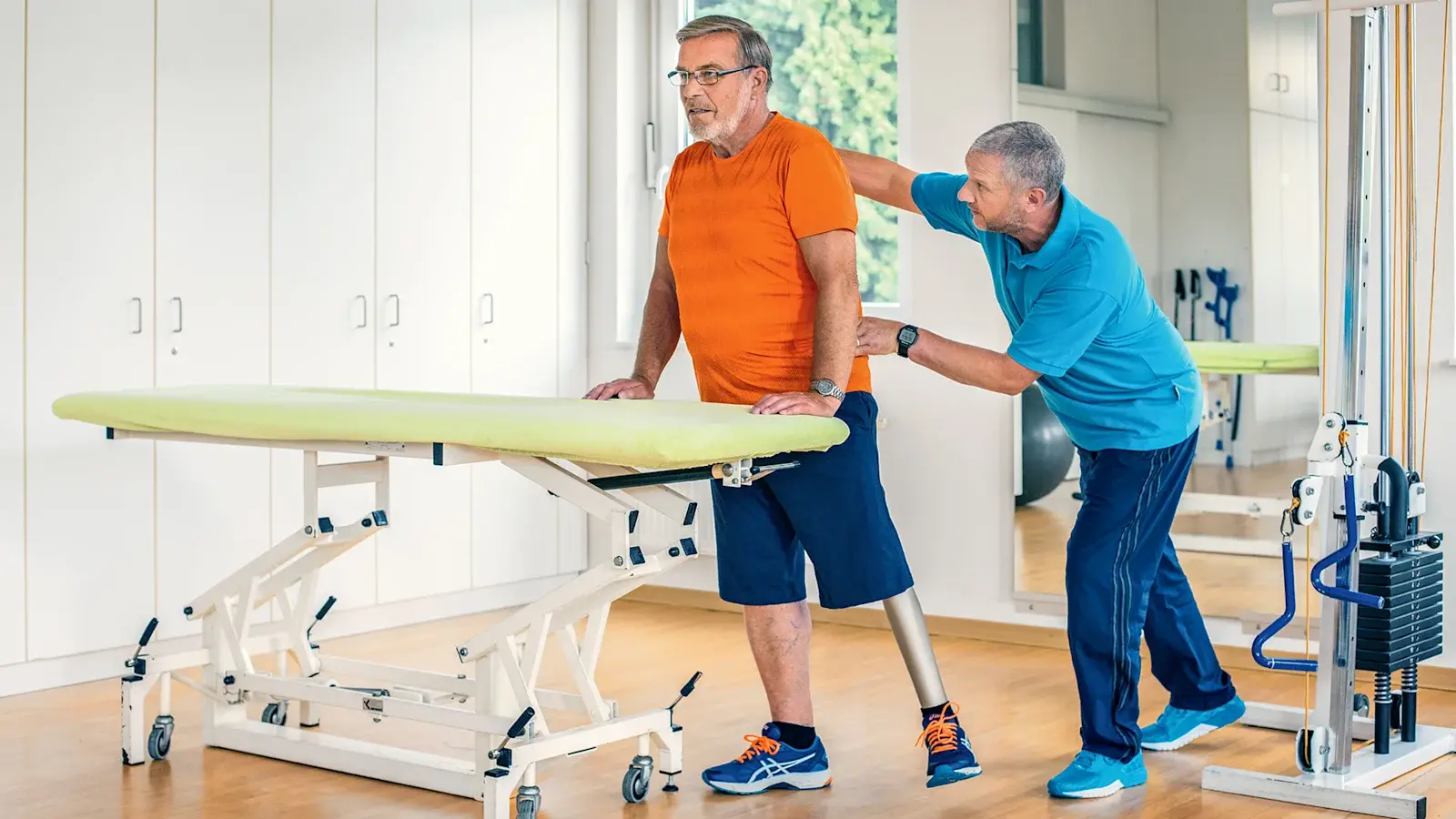 A clinician supporting a man wearing an above-knee prosthesis during a trial fitting